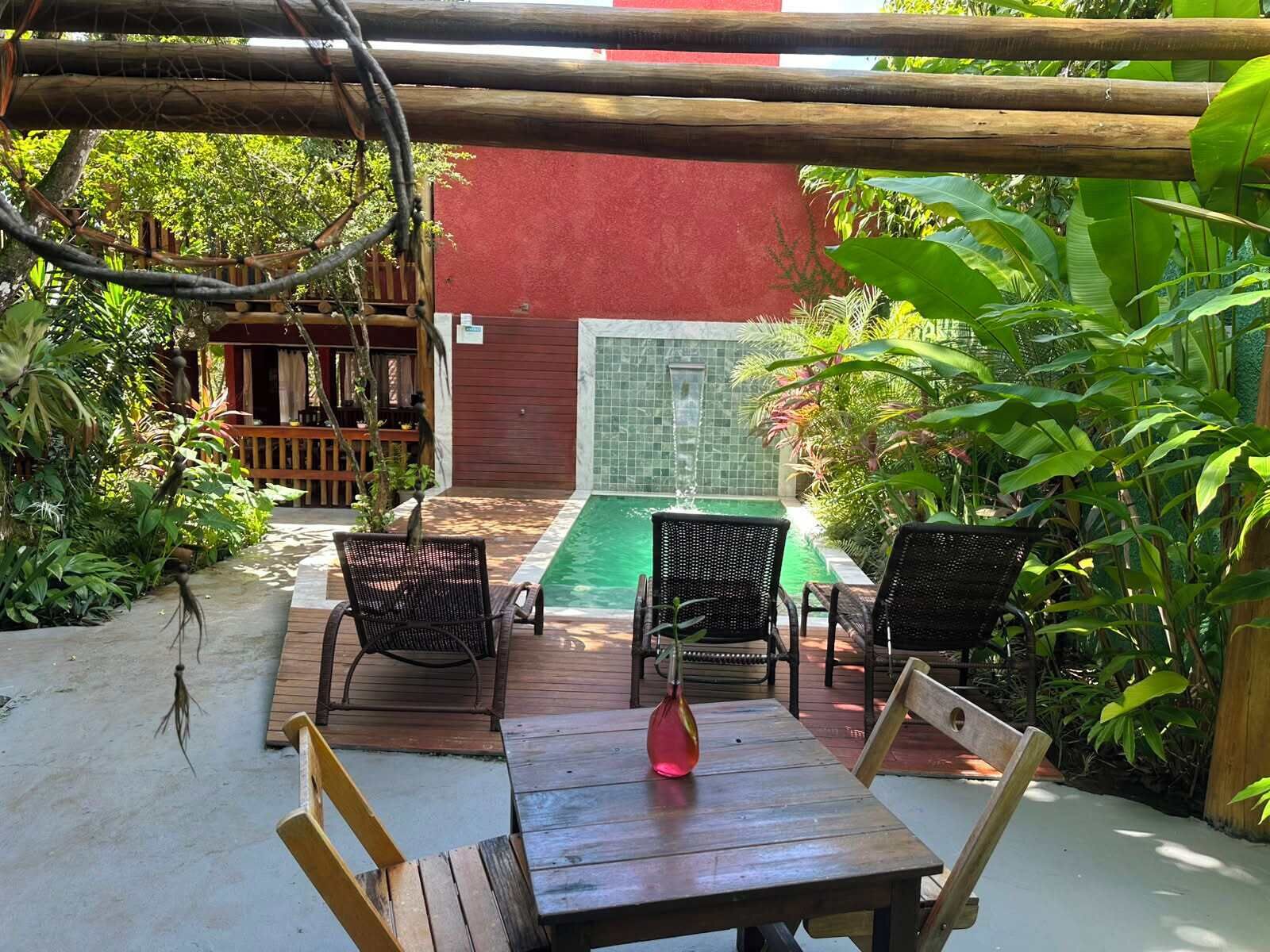 A patio with a pool, outdoor furniture, and lush greenery.