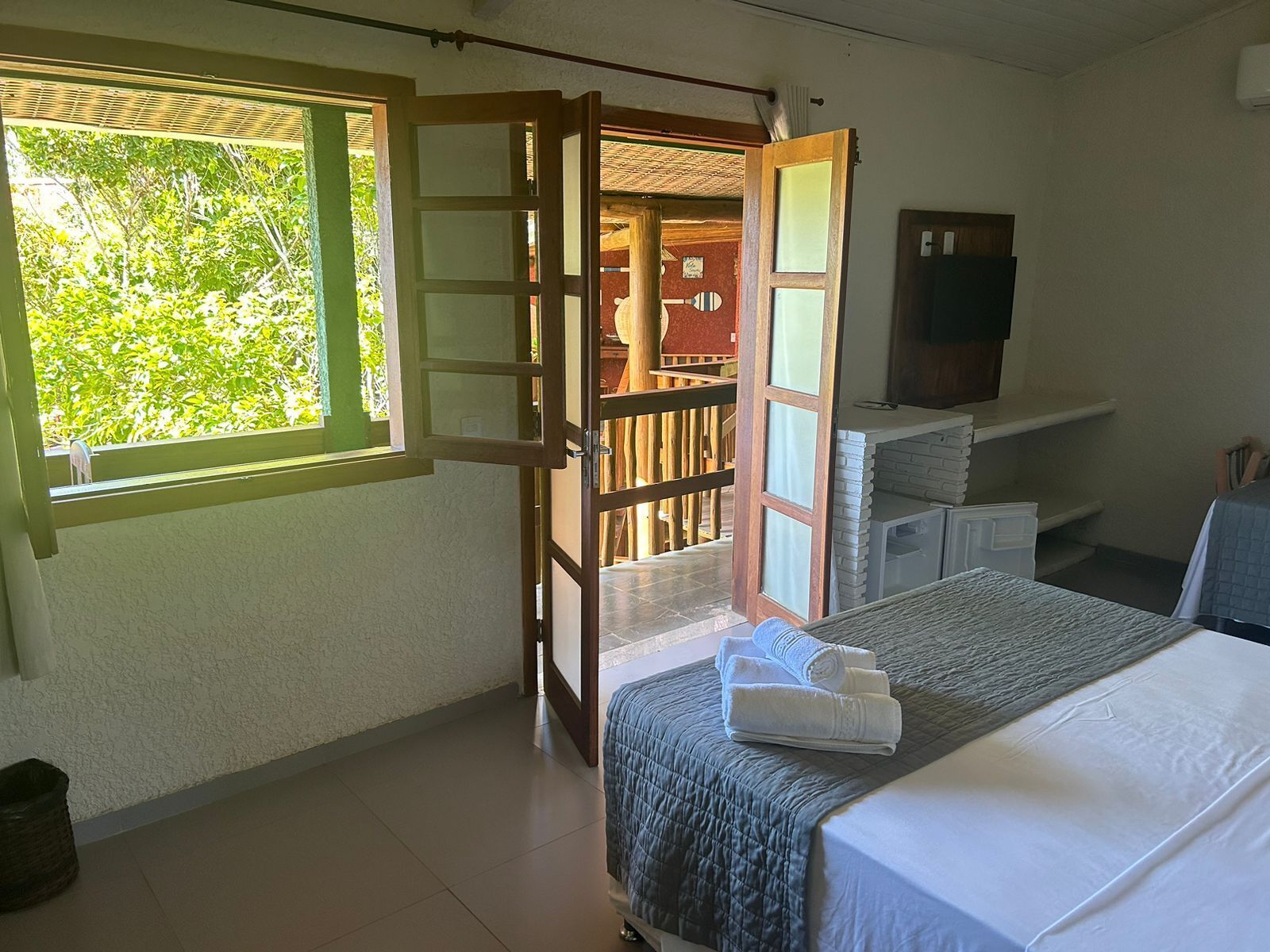 A bedroom with a bed, a window, a door leading outside, and a small table with towels.