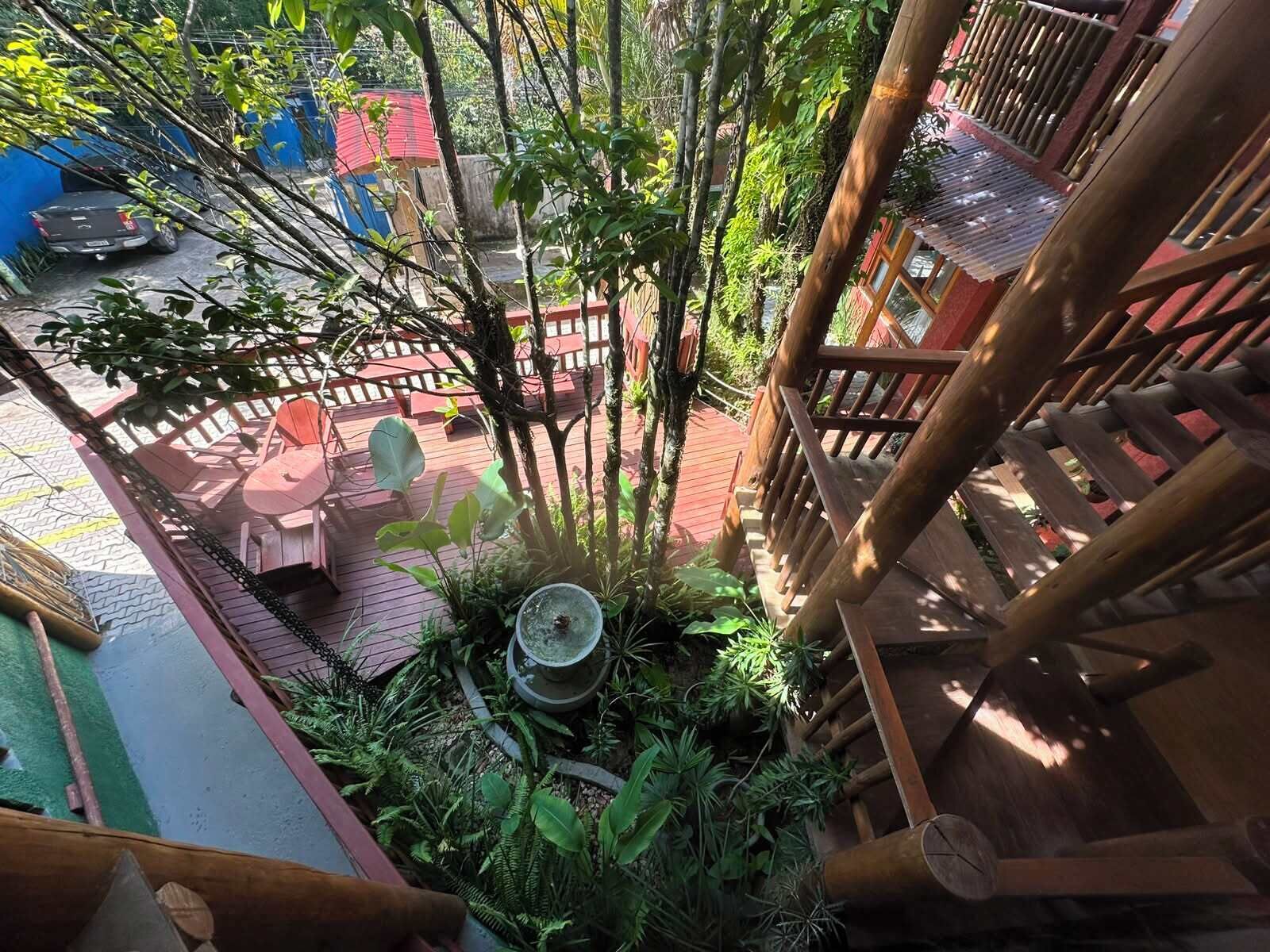 Una escalera de madera que conduce a un balcón con vistas a un jardín, una valla roja y un coche aparcado.