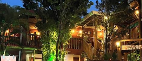 Un hotel con fachada de madera, un espacio exterior cubierto con luces colgantes y un letrero que dice 'SUAEM BEM VINDOS!'.