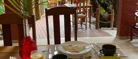 A breakfast setting with a table set for two, including plates, bowls, cutlery, and a bottle of juice.