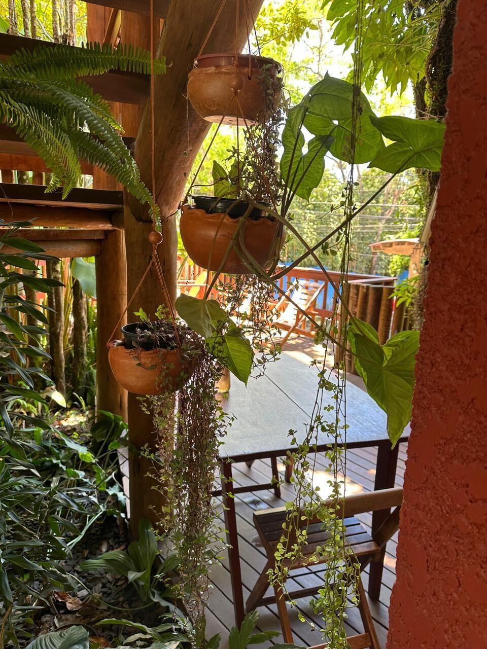 A wooden deck with hanging terracotta pots containing various plants, a wooden railing, and a view of a garden area.