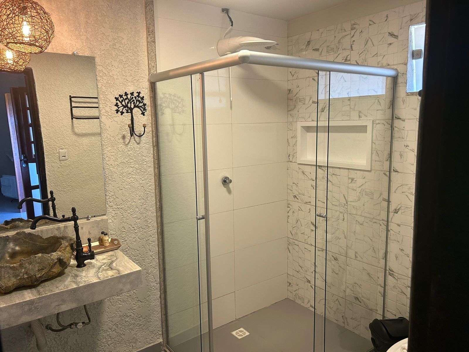 A bathroom with a stone sink, a glass shower enclosure, and a marble-tiled wall.