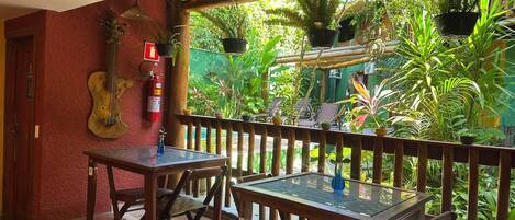 A wooden table and chairs on a veranda with a view of lush greenery.
