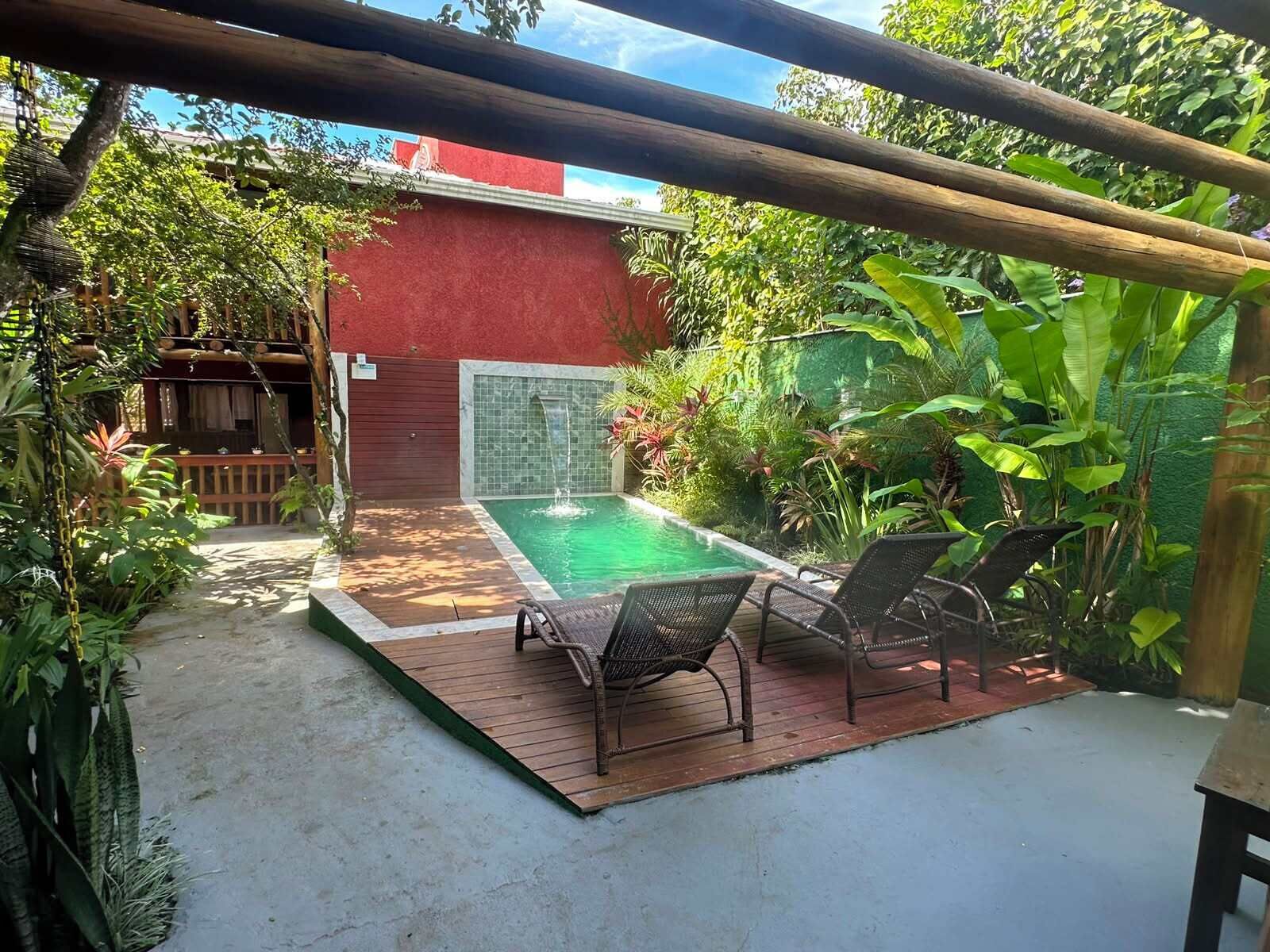 A pool area with a wooden deck, two lounge chairs, and a small waterfall feature.