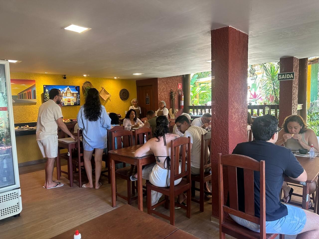 A restaurant with wooden tables and chairs, a counter, and a mural on the wall.