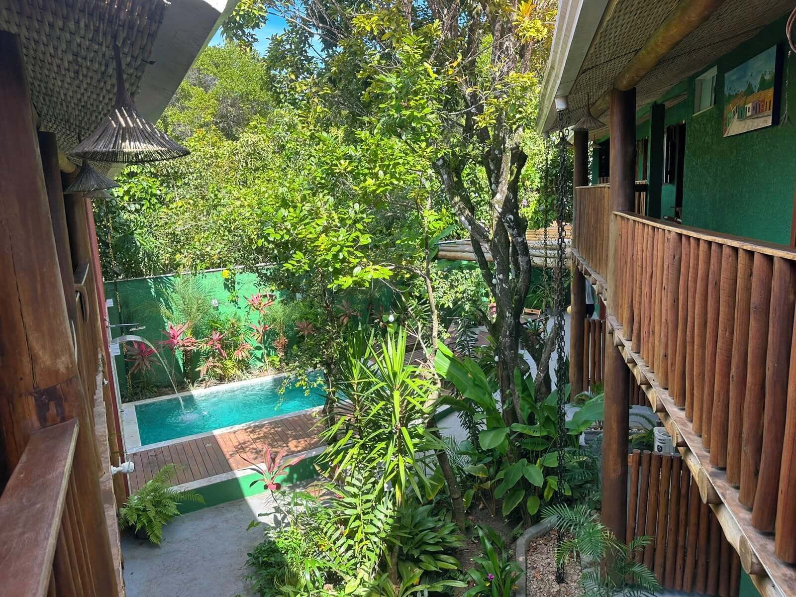 A pool surrounded by lush greenery, wooden fences, and a green wall with a painting.