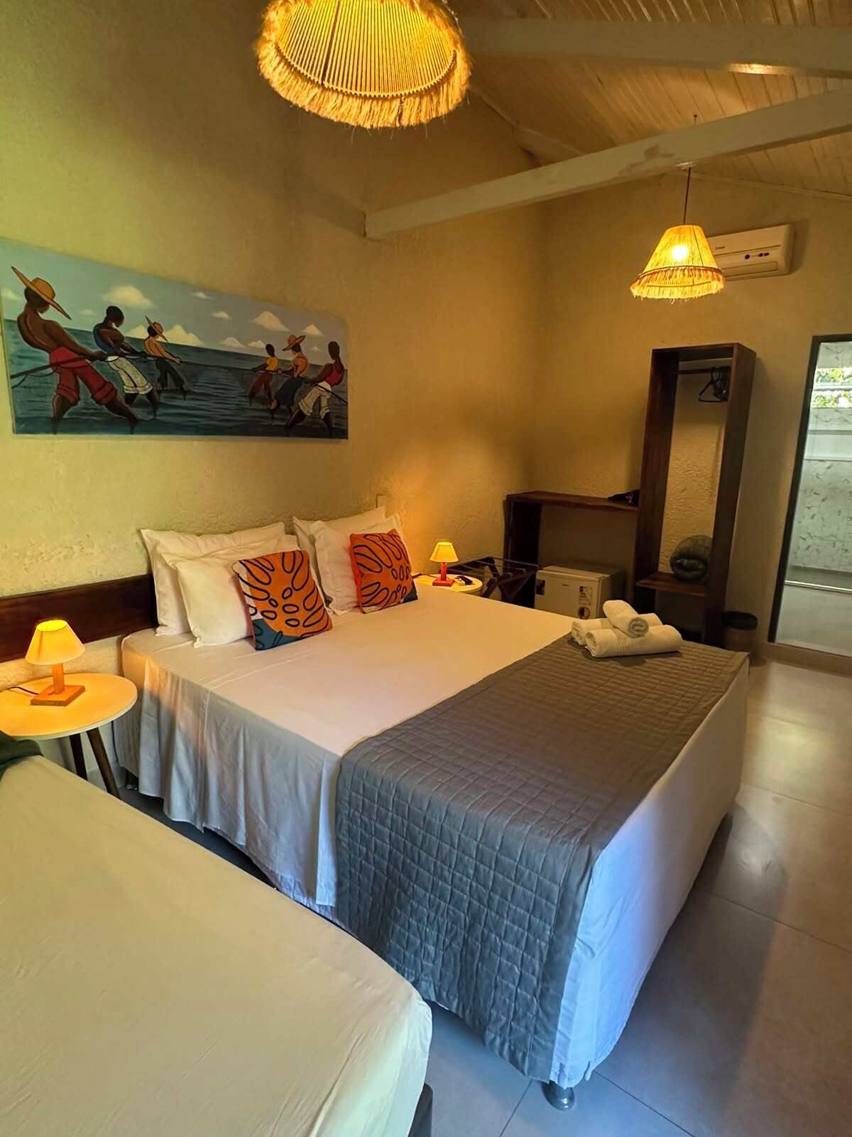 A hotel room with a bed, bedside tables, a painting, a mirror, and a window.