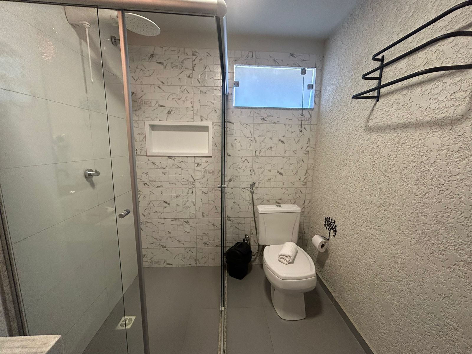 Kylpyhuoneessa on lasiseinäinen suihkukaappi, wc ja pieni ikkuna.