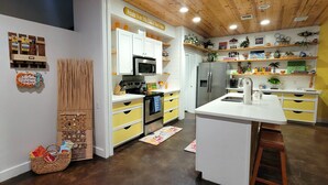 Una cocina con techo de madera, armarios amarillos, una isla central y un refrigerador de acero inoxidable.