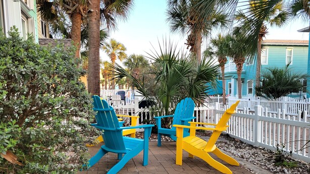 Un patio con dos sillas Adirondack, una cerca blanca de piquetes y una palmera.