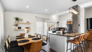 A modern kitchen with white cabinets, a central island, and a dining area with a wooden table and chairs. - Modern Close to Denver 4bdr Home-Great for groups (Arvada)