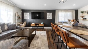 A modern living room with a sofa, coffee table, and a TV mounted on the wall. - Modern Close to Denver 4bdr Home-Great for groups (Arvada)