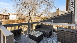A covered outdoor patio with wicker furniture and a glass table. - Modern Close to Denver 4bdr Home-Great for groups (Arvada)