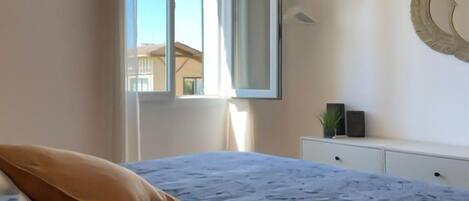 A bedroom with a bed, a window, a bedside table, and a mirror.