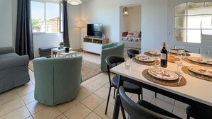 Een moderne woonkamer met een bank, een eettafel voor vier personen en een televisie op de achtergrond.