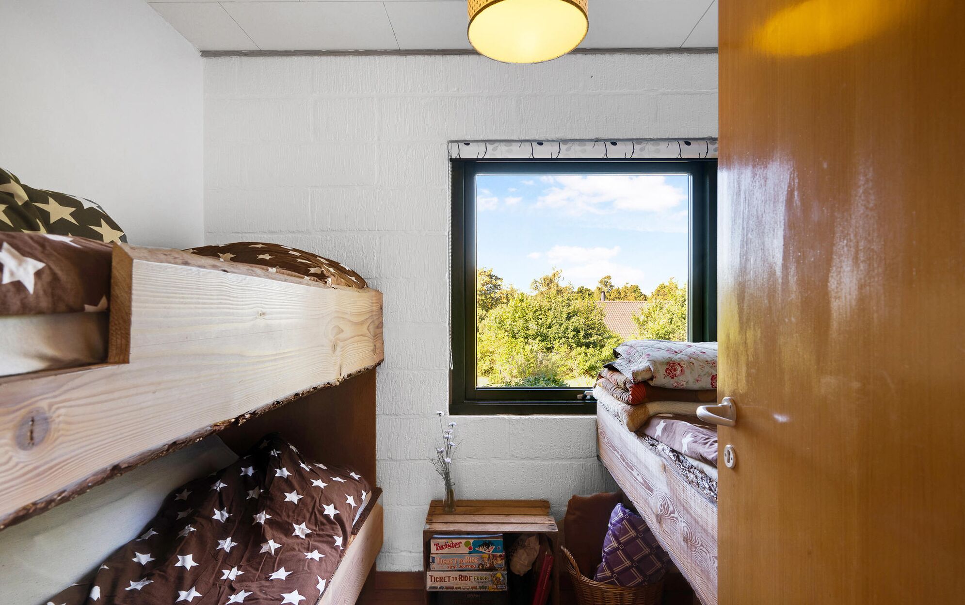 Dormitorio con literas, una ventana, una mesa pequeña con un florero y un cabecero de madera.