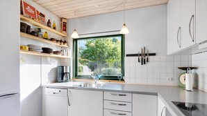 Una cucina moderna con mobili bianchi, forno integrato, macchina del caffè e una finestra vista verdeggiante.