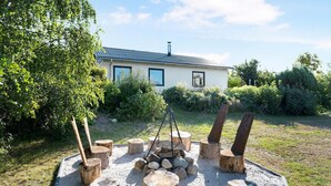 Una casa con tetto in metallo, un camino e un giardino con un focolare circondato da tronchi d'albero.