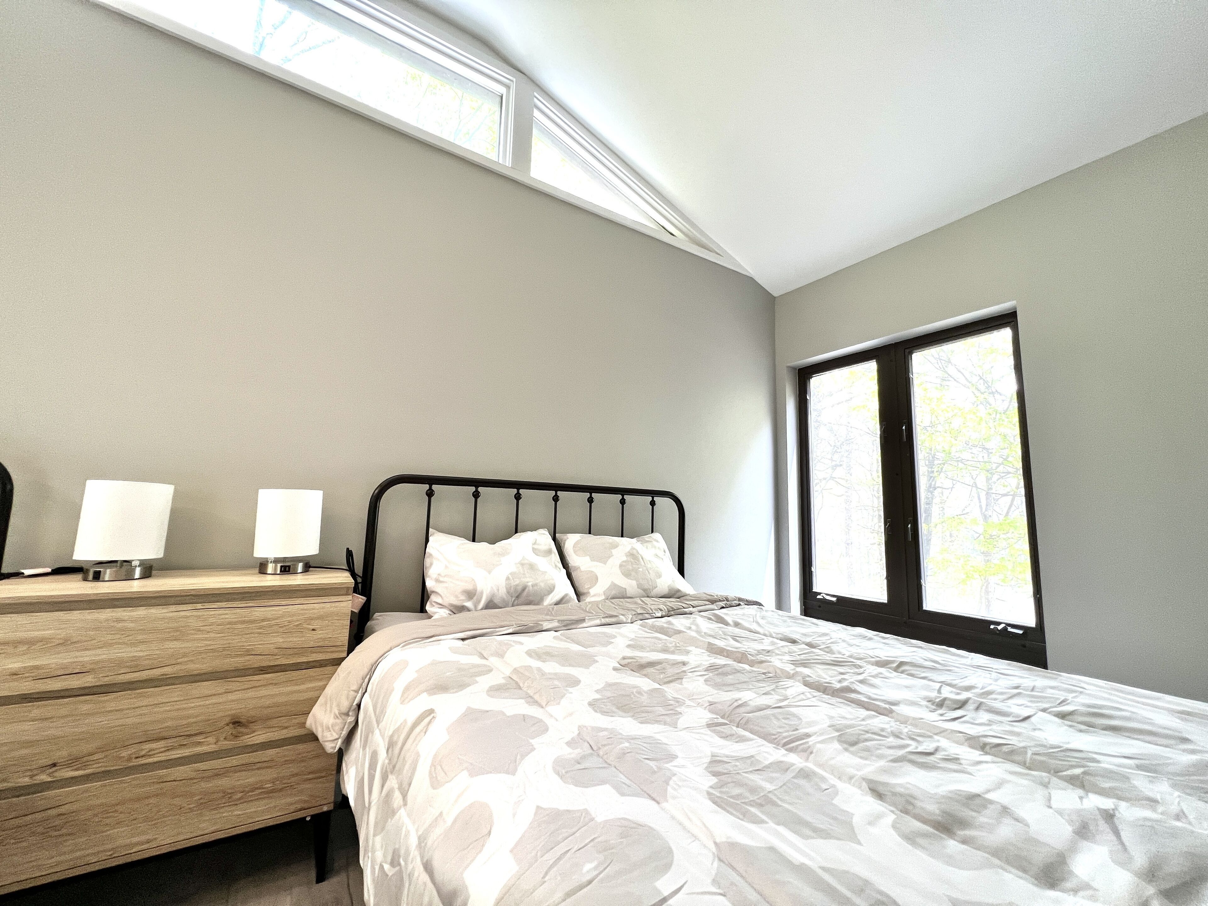 A bedroom with a bed, a nightstand, a dresser, and a window with a view of trees.