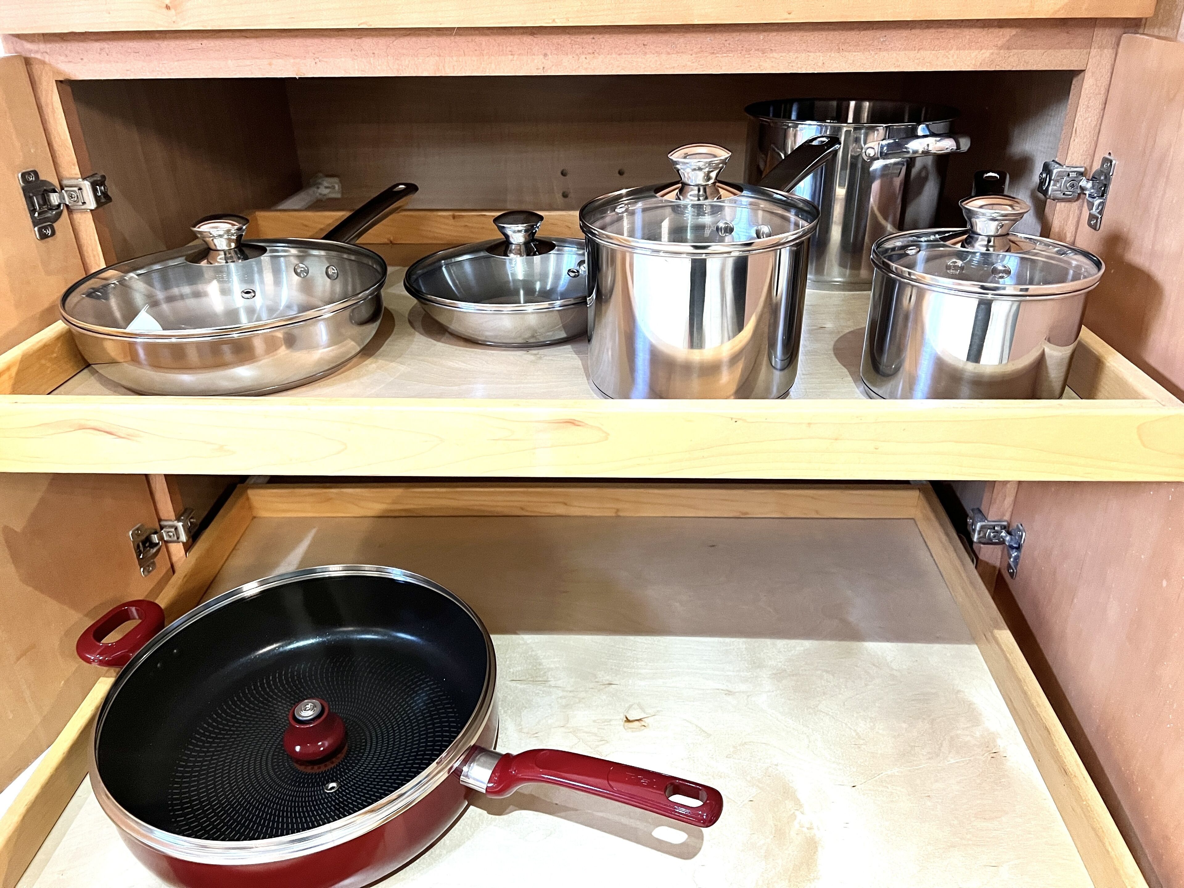 Ein Küchenschrank mit Edelstahlkochgeschirr, darunter Töpfe, Pfannen und eine Bratpfanne.