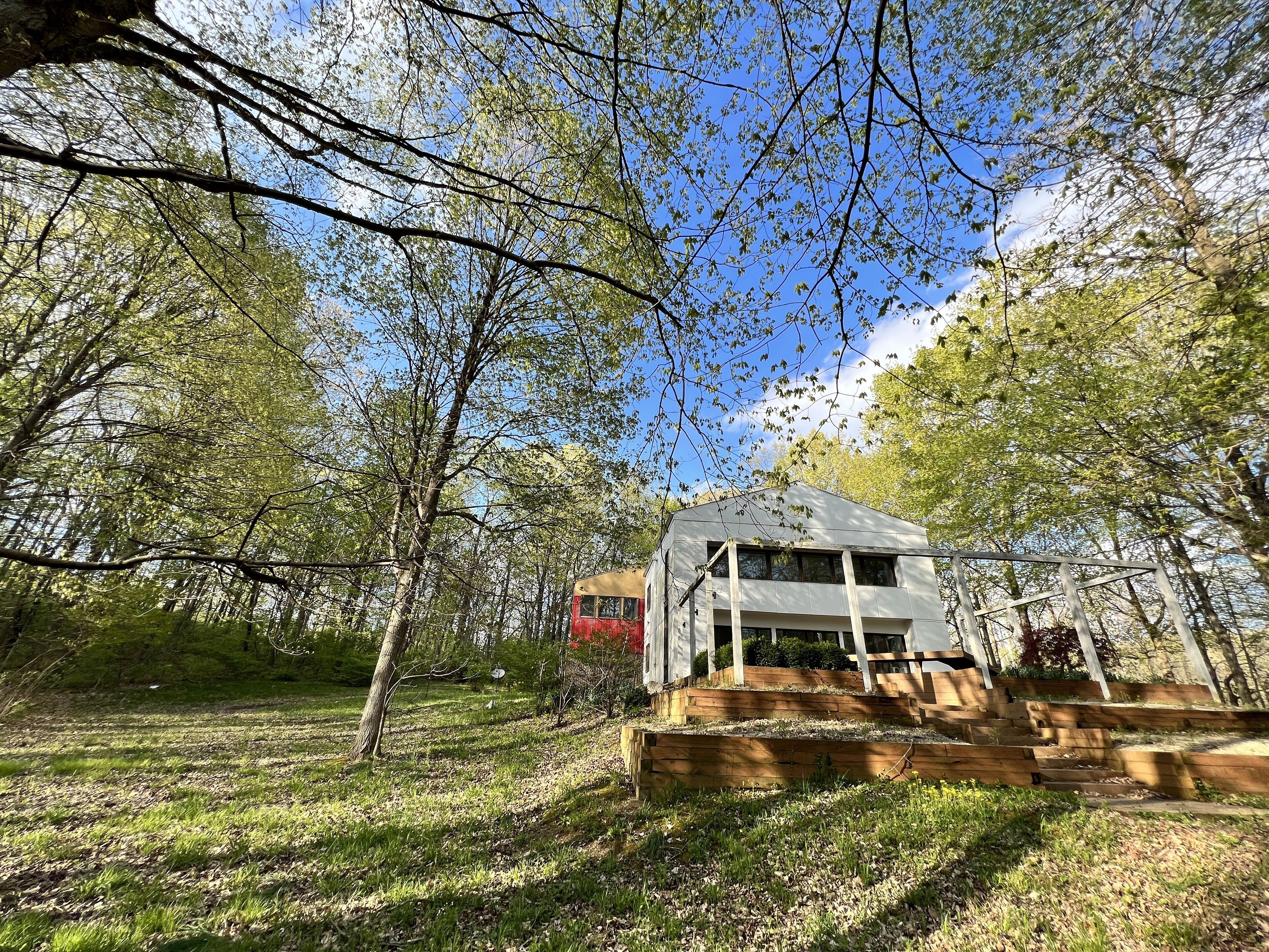 Une maison avec un toit en pente, entourée d’une zone boisée avec des arbres et une pelouse.