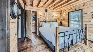 Quarto de cabana de madeira com uma cama, um relógio de parede e uma janela.