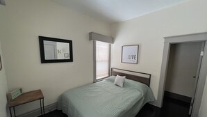 Quarto com cama, mesa de cabeceira, espelho, janela e porta.