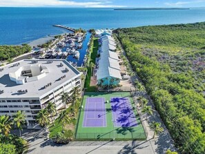 Vista aérea de un resort con cancha de tenis, área de piscina y un edificio con varios balcones.