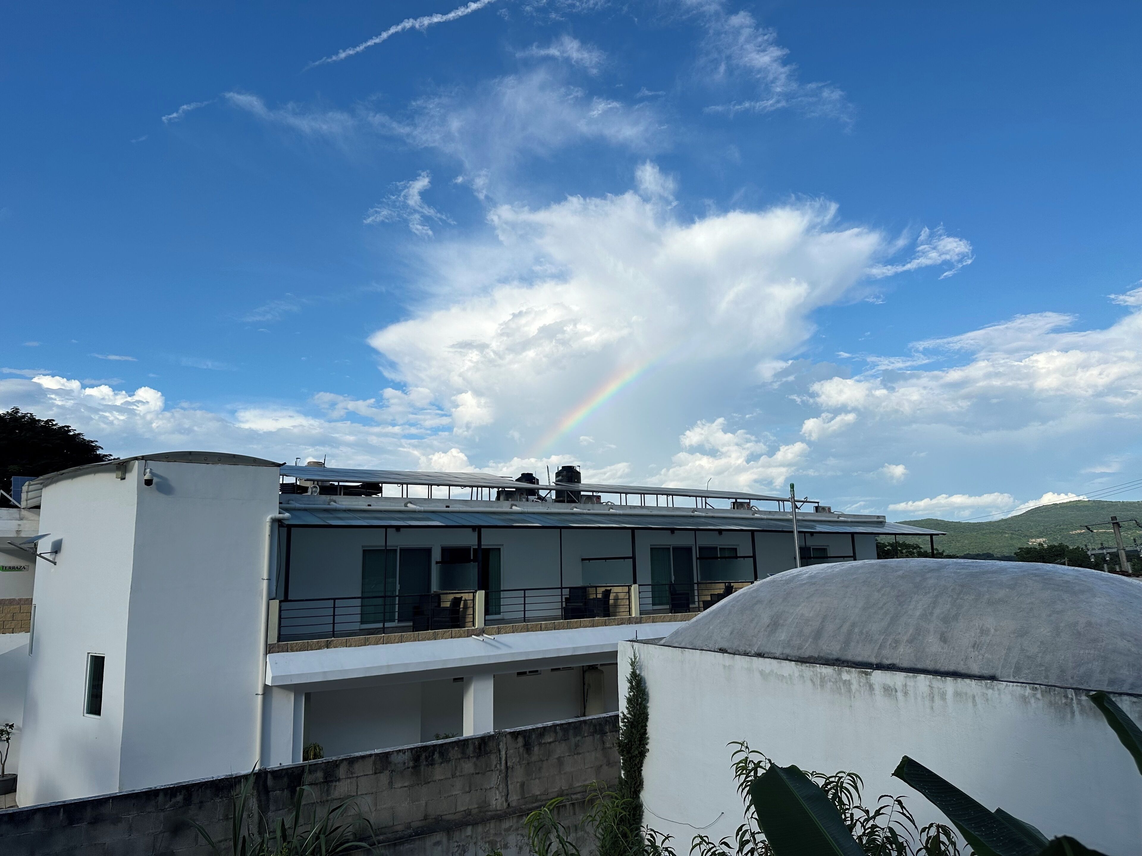En modern byggnad med ett platt tak, stora fönster och en tydlig regnbåge synlig på himlen.