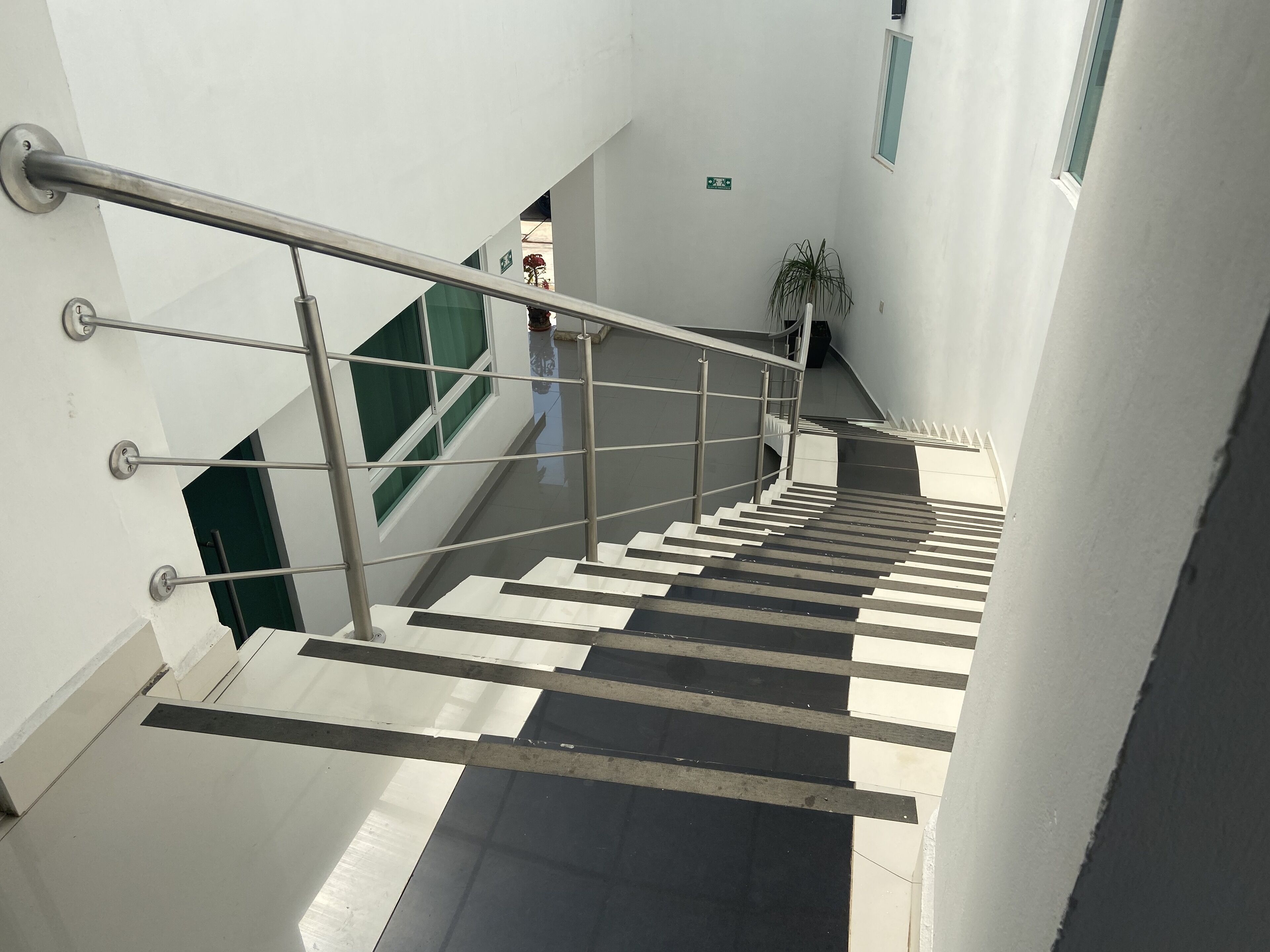 A modern interior with a metal handrail, white walls, and a staircase with alternating black and white steps.