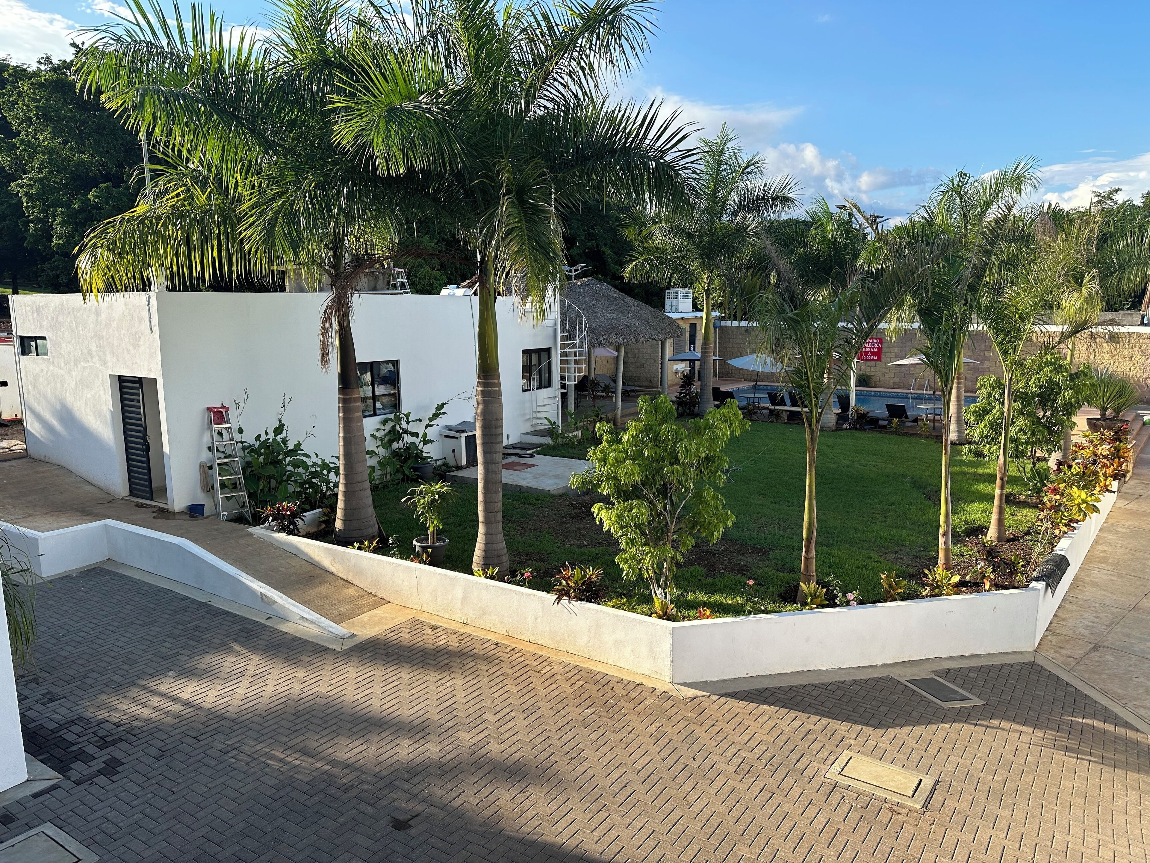 A modern building with a white exterior, surrounded by a well-maintained garden with palm trees and a grassy lawn.