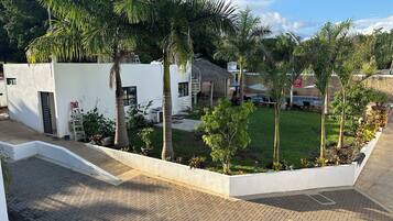 A modern building with a white exterior, surrounded by a well-maintained garden with palm trees and a grassy lawn.