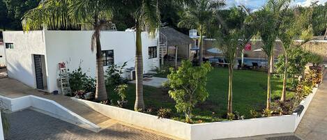 A modern building with a white exterior, surrounded by a well-maintained garden with palm trees and a grassy lawn.