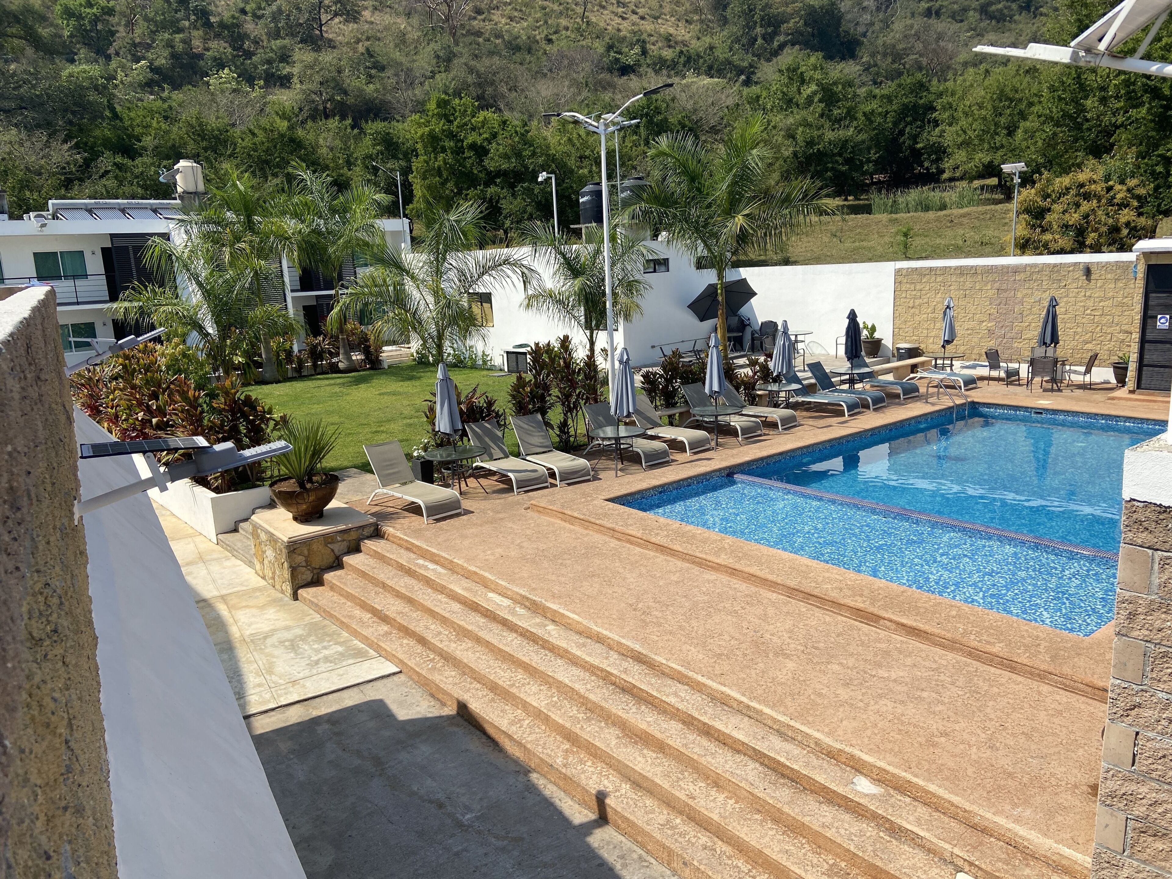 A swimming pool with sun loungers and a small table, surrounded by steps and potted plants.
