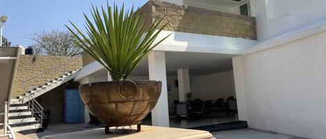 Un edificio moderno con un gran macizo de plantas en el patio, una escalera y un área de descanso con mesas y sillas.