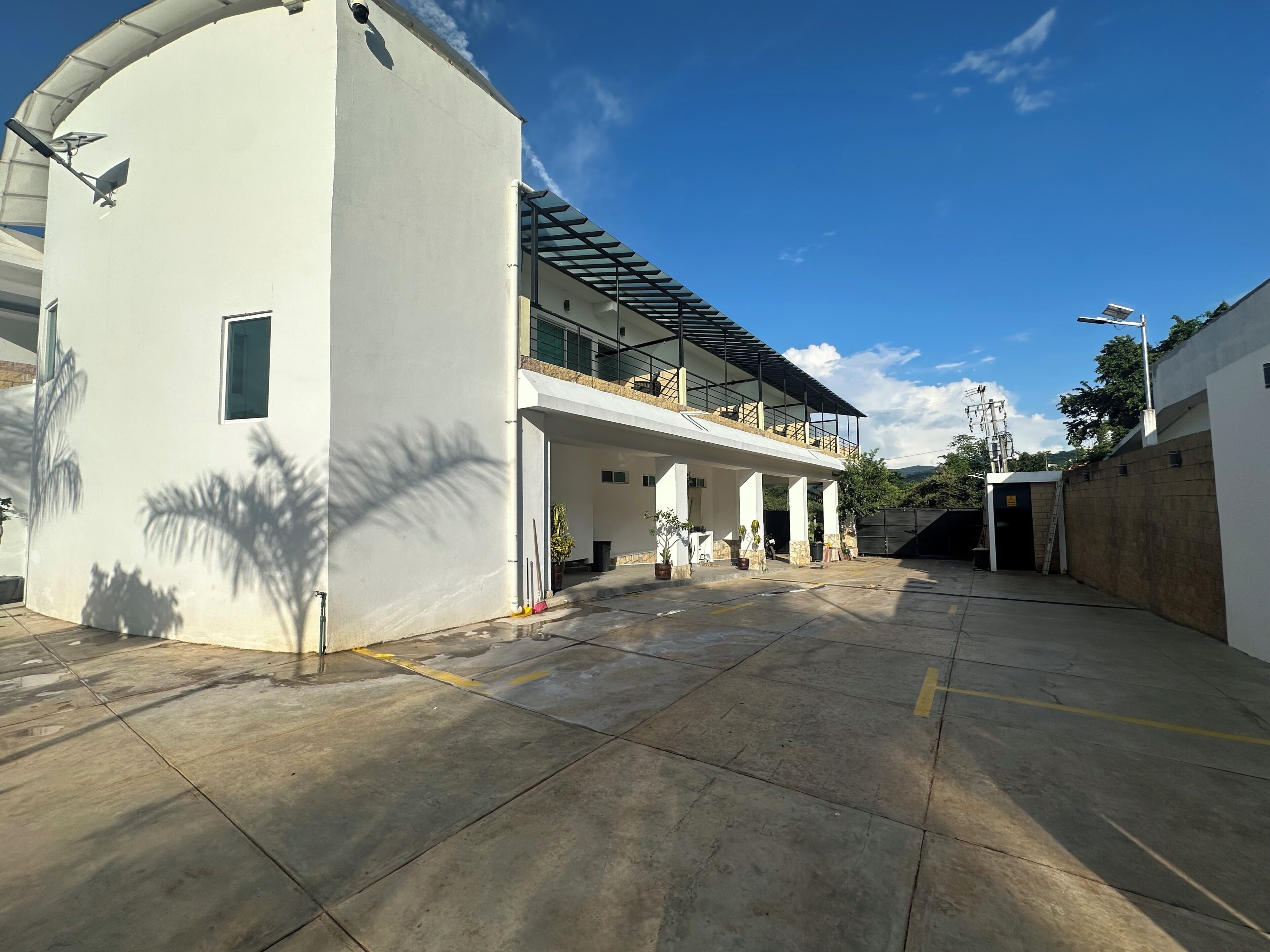 A spacious outdoor area with a covered seating area, a building with a balcony, and a clear blue sky.