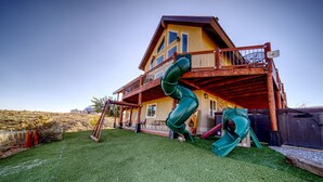Une maison à deux étages avec une terrasse en bois et un toboggan vert.
