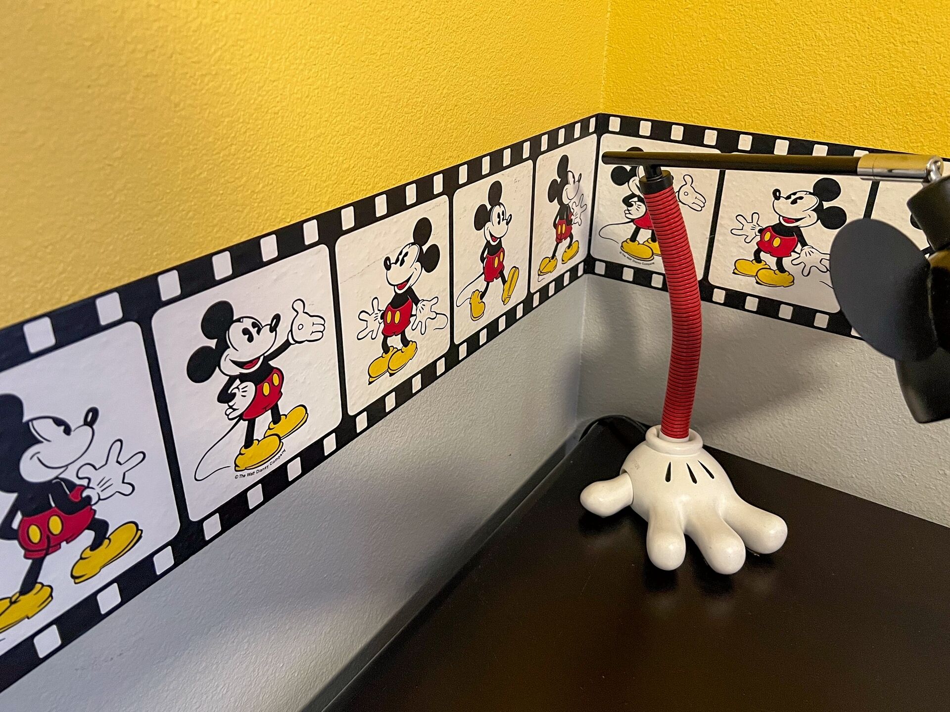 Eine Ecke mit Wanddekoration zum Thema Mickey Mouse und einer Mickey-Mouse-förmigen Schreibtischlampe.