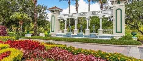 A sign for Emerald Island Resort with a white structure, green accents, and a garden with colorful flowers.