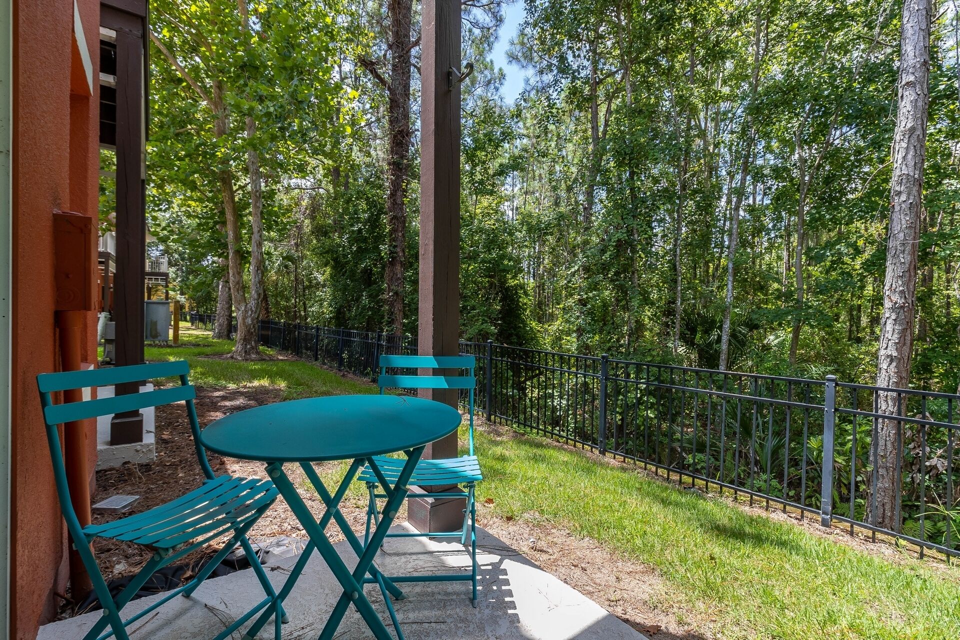 An outdoor seating area with a table and chairs, surrounded by a metal fence and trees.