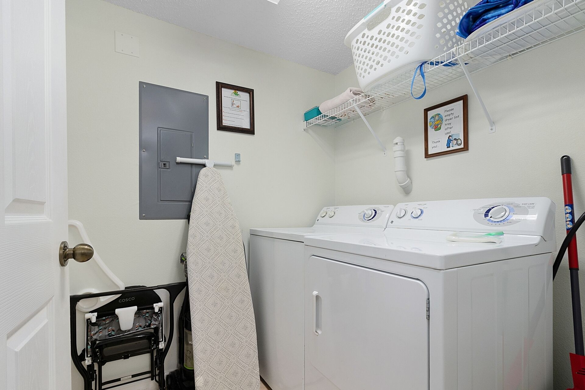 A laundry room with a front-loading washer and dryer, a drying rack, a wall-mounted drying machine, and a door with a towel hanging on it.