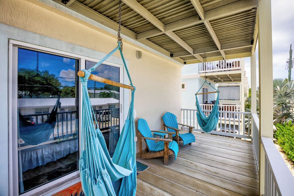 A wooden deck with two hammocks and two blue chairs.