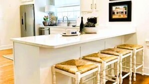 Uma cozinha moderna com armários brancos, uma ilha central com banquetas e uma janela grande que traz luz natural.