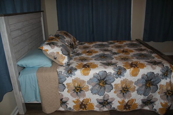 A bedroom with a wooden headboard, a floral bedspread, a blue pillow, and a beige blanket.