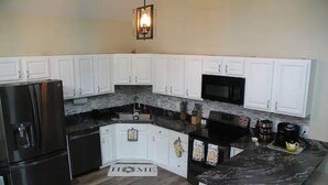Una cocina moderna con armarios blancos, un refrigerador negro, un microondas y una cafetera.
