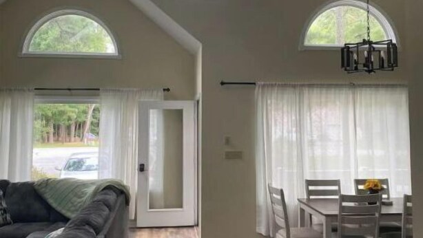 Una habitación amplia con techo alto, ventilador de techo y dos grandes ventanas que proporcionan luz natural. Cuenta con un comedor con mesa y sillas, y un sofá en la sala.