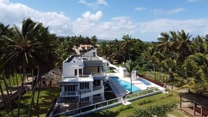 A modern multi-story building with a pool, surrounded by palm trees and greenery. - Beautiful Beach Condo on the sand (Cabarete)