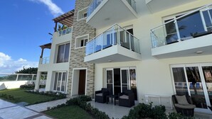 A modern multi-story residential building with a stone facade, large glass balconies, and a well-maintained lawn. - Beautiful Beach Condo on the sand (Cabarete)