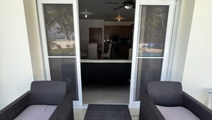 A balcony with two wicker chairs and a small table, leading to a kitchen and dining area with a ceiling fan. - Beautiful Beach Condo on the sand (Cabarete)